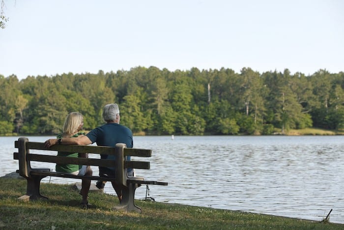 two people sitting on a bench before a lake